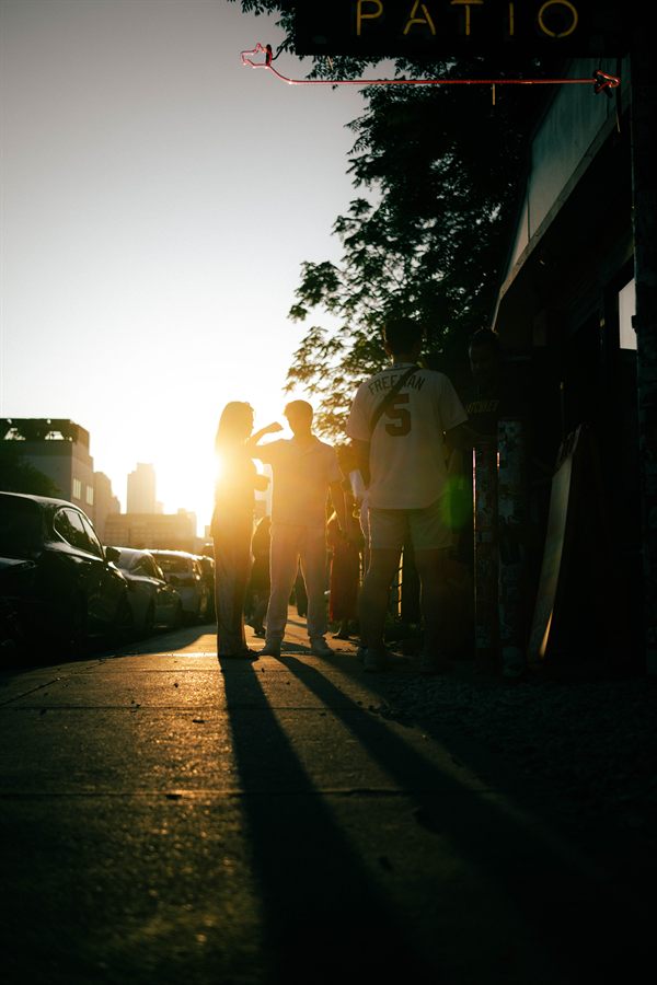 Silhouetted people outside a patio, the low sun bursting behind them and long shadows ahead.
